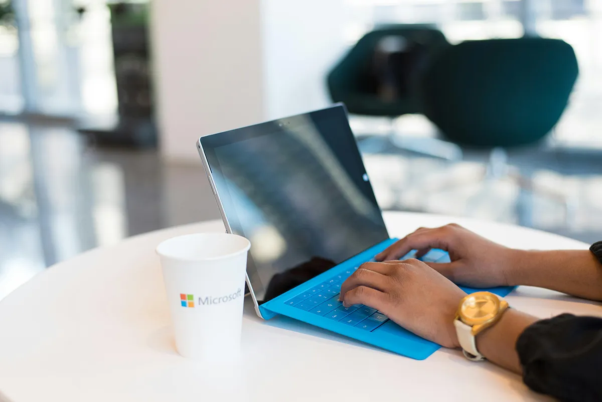 Free Microsoft Nonprofit Licenses to End in 2025 microsoft 365 changes. a woman working on a windows laptop at a desk with a take away coffee cup